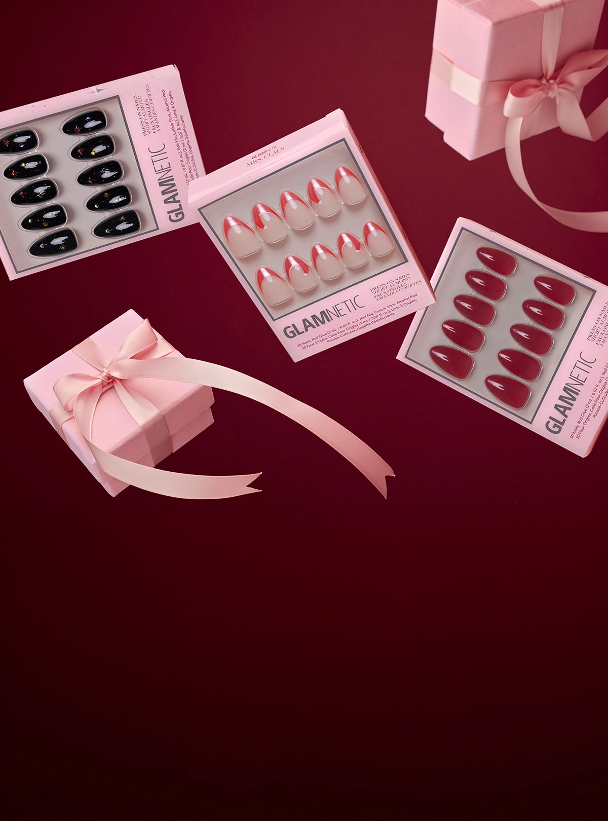 Glamnetic holiday press-on nail sets displayed on a red background with pink ribbon gift boxes.