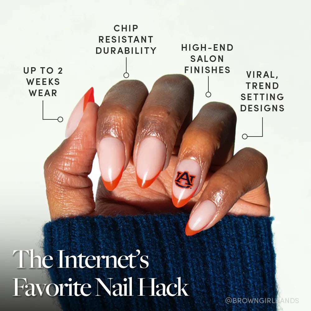 A hand with long, almond-shaped nails features the Auburn Tigers Press-On Nail Set by glamnetic, showcasing a French tip and "AU" logo. Enjoy up to 2 weeks of chip-resistant wear, high-end finishes, and viral trendsetting designs. - Product image