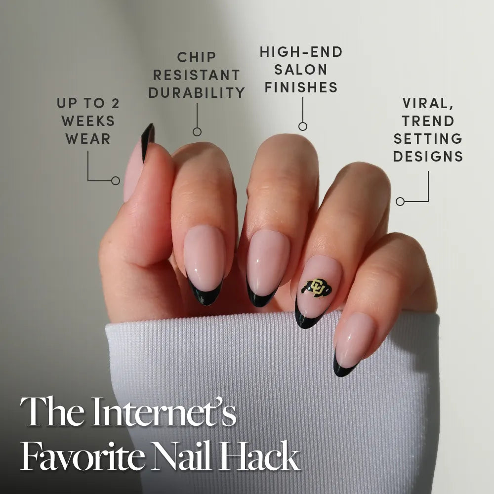 A hand with long, almond-shaped nails featuring a natural base, black French tips, and a gold accent design showcases glamnetic’s Colorado Buffaloes Press-On Nail Set—salon-quality, viral designs, durable wear for up to two weeks. - Product image
