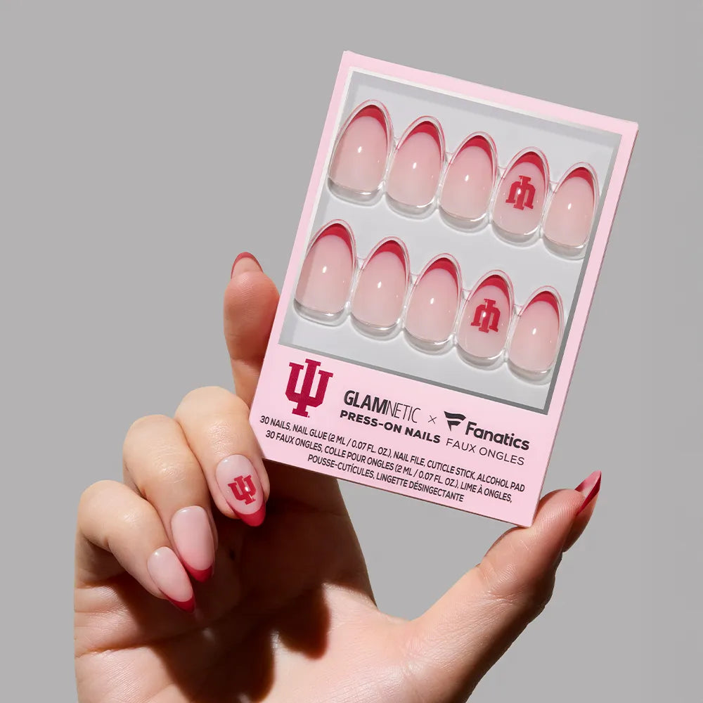 A hand holds the glamnetic Indiana Hoosiers Press-On Nail Set, showcasing crimson French tip nails with the team logo in a pink and white box featuring glamnetic and Fanatics branding.