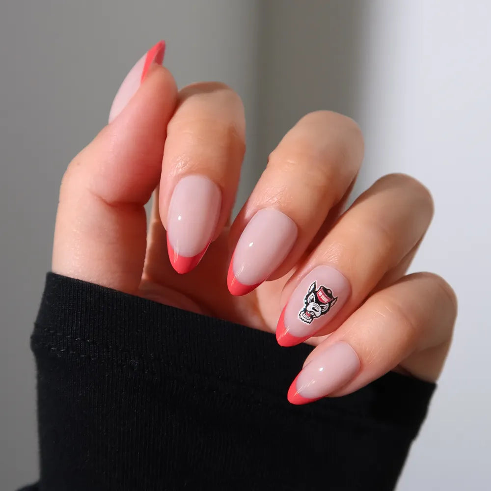 The NC State Wolfpack Press-On Nail Set by glamnetic features almond-shaped nails with a light pink base and bright red French tips, plus a nail with a tiny cartoon face. The nails are shown on a hand partially covered by a black sleeve. - Product image