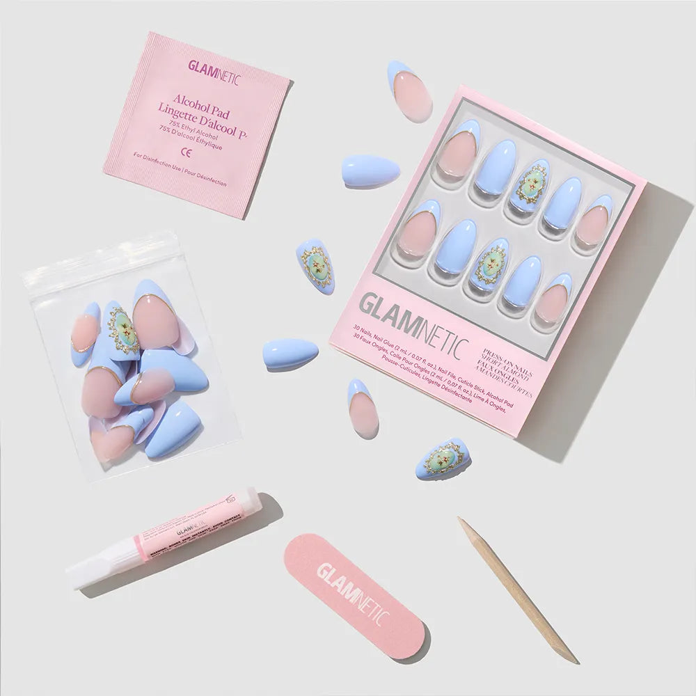 A flat lay of glamnetic's Angel in Blue press-on nails kit, featuring blue and pink short almond nails, nail glue, cuticle stick, pink file, alcohol pad, and extra nails—all neatly arranged on a light background. - Product image