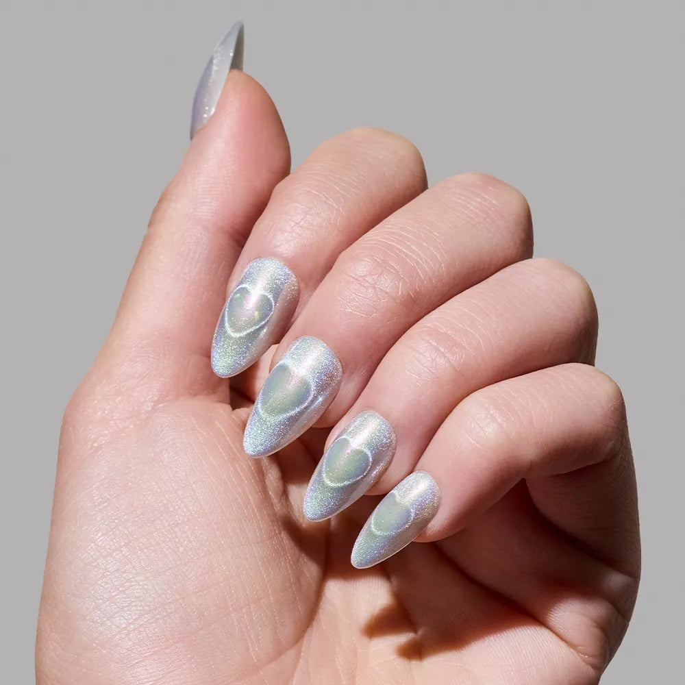 A hand flaunts long, almond-shaped holographic nails by glamnetic in the shade Electric Lover, each with a subtle raised heart design atop shimmery iridescent polish, set against a plain gray background. - Product image
