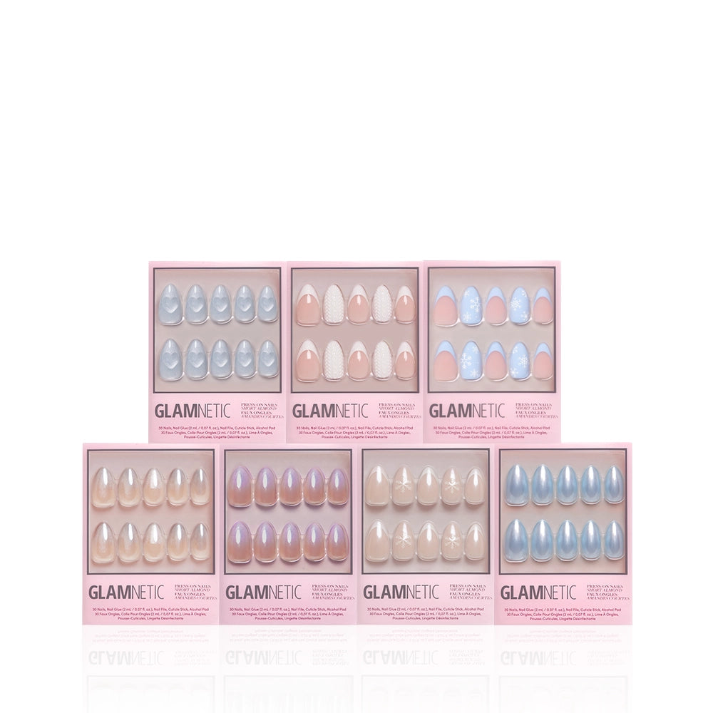 Seven boxes of glamnetic Frozen Over press-on nails are arranged in two rows. Each box shows a short almond set in pastel pink, lavender, blue, and nude shades, with some sets featuring winter designs and snowflake accents. - Product image