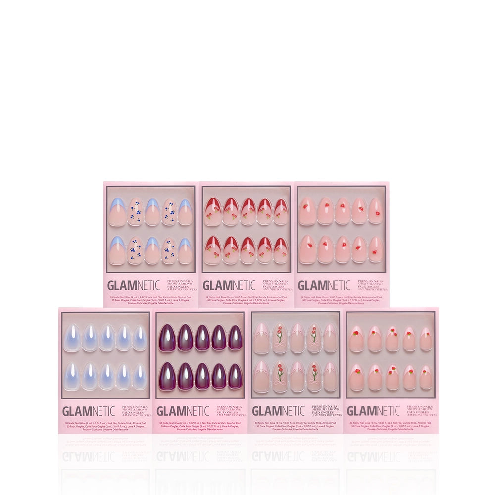 Seven boxes of glamnetic Freshly Picked press-on nails in assorted pastel and floral designs are arranged in two rows on a white background, each showing off glossy or trendy short almond sets through clear windows. - Product image