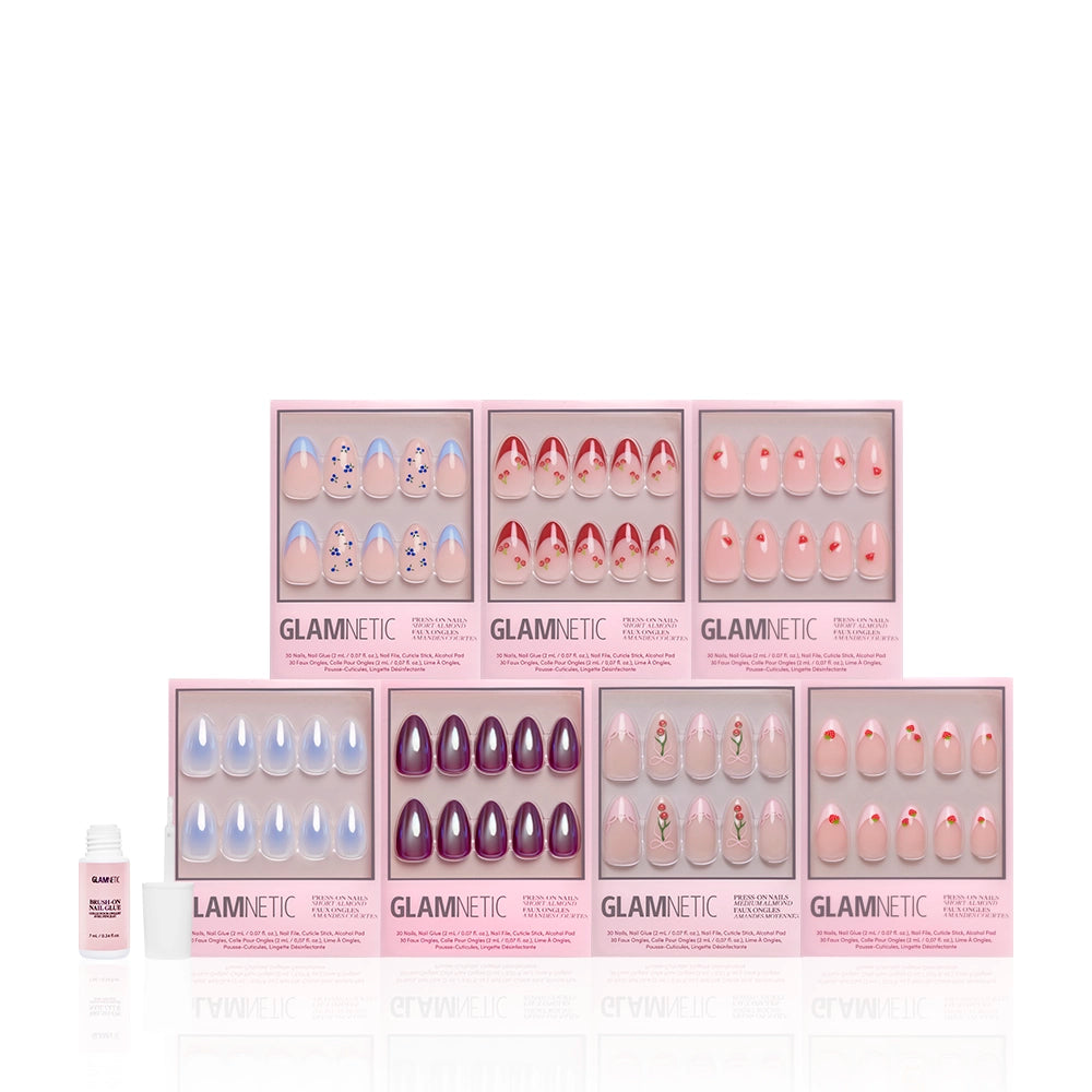 Eight sets of glamnetic Freshly Picked press-on nails with colorful designs and glossy finishes are neatly arranged in pink packaging, featuring trendy French tips and short almond shapes. A small bottle of nail glue sits to the left. - Product image