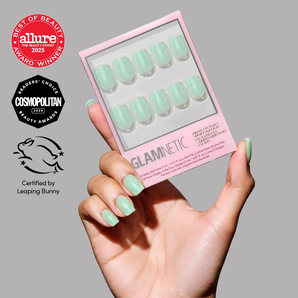 A hand with mint green press-on nails holds a box of glamnetic’s Honeydewy vegan, cruelty-free nails in the same mint shade. Award logos from Allure, Cosmopolitan, and Leaping Bunny are shown on the gray background.