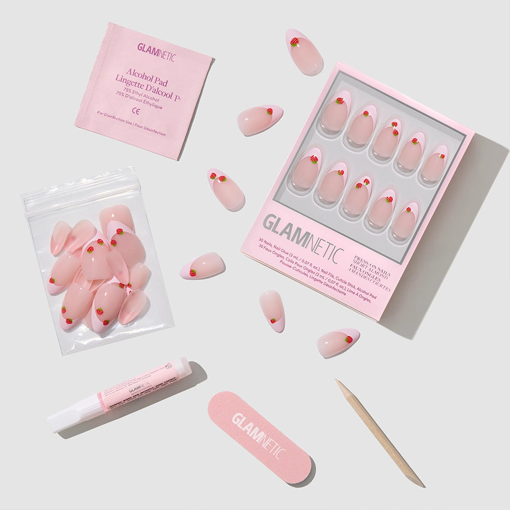 The glamnetic Strawberry Bits set features pink almond press-on nails with red hearts, nail glue, a cuticle stick, nail file, alcohol pad, and extra nails—all neatly arranged on a light background. - Product image