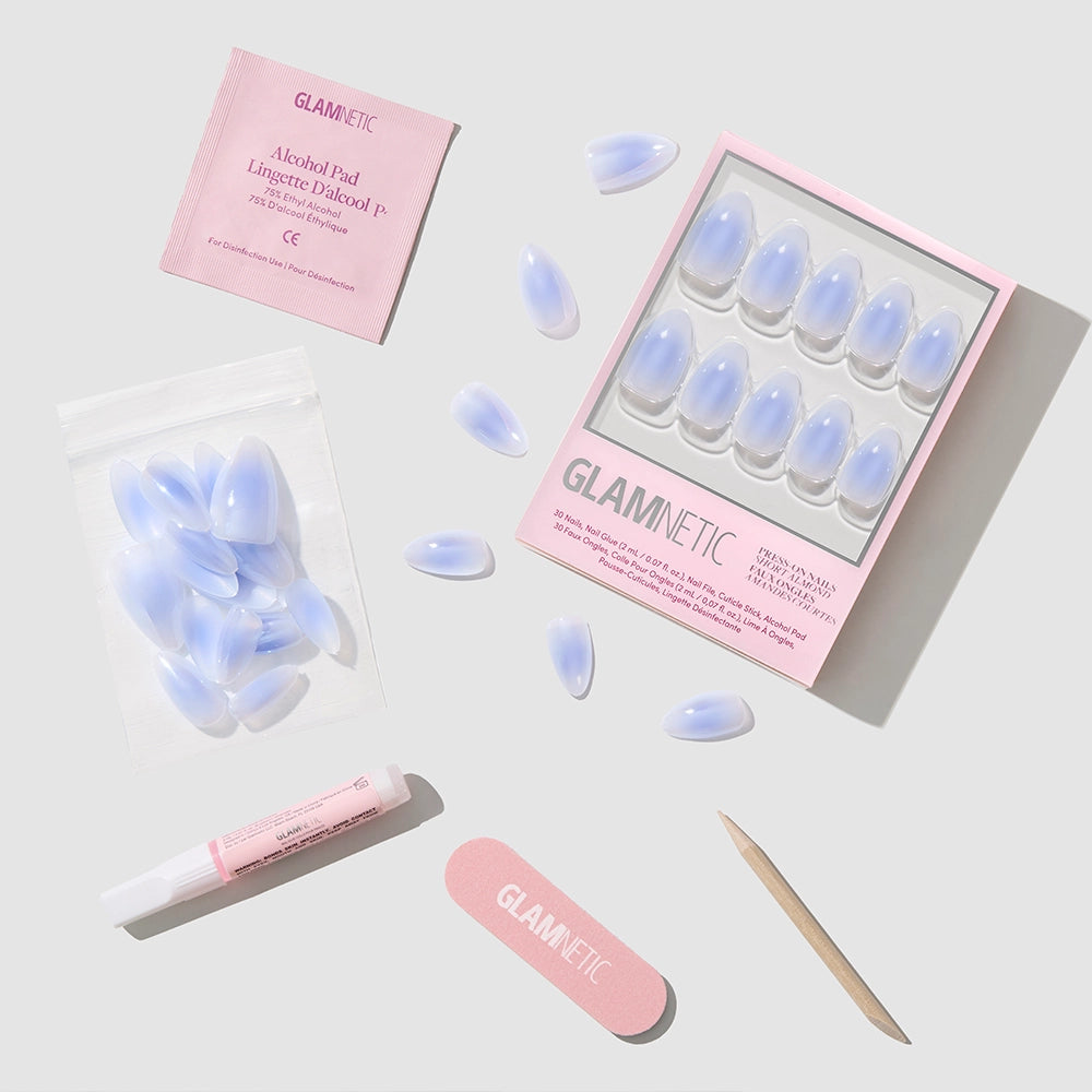 The Sky Berry press-on nail kit by glamnetic features pastel blue almond nails with a glazed finish, an alcohol pad, glue, nail file, cuticle stick, and extra nails—arranged on a light gray background. Packaging and file show the glamnetic logo. - Product image