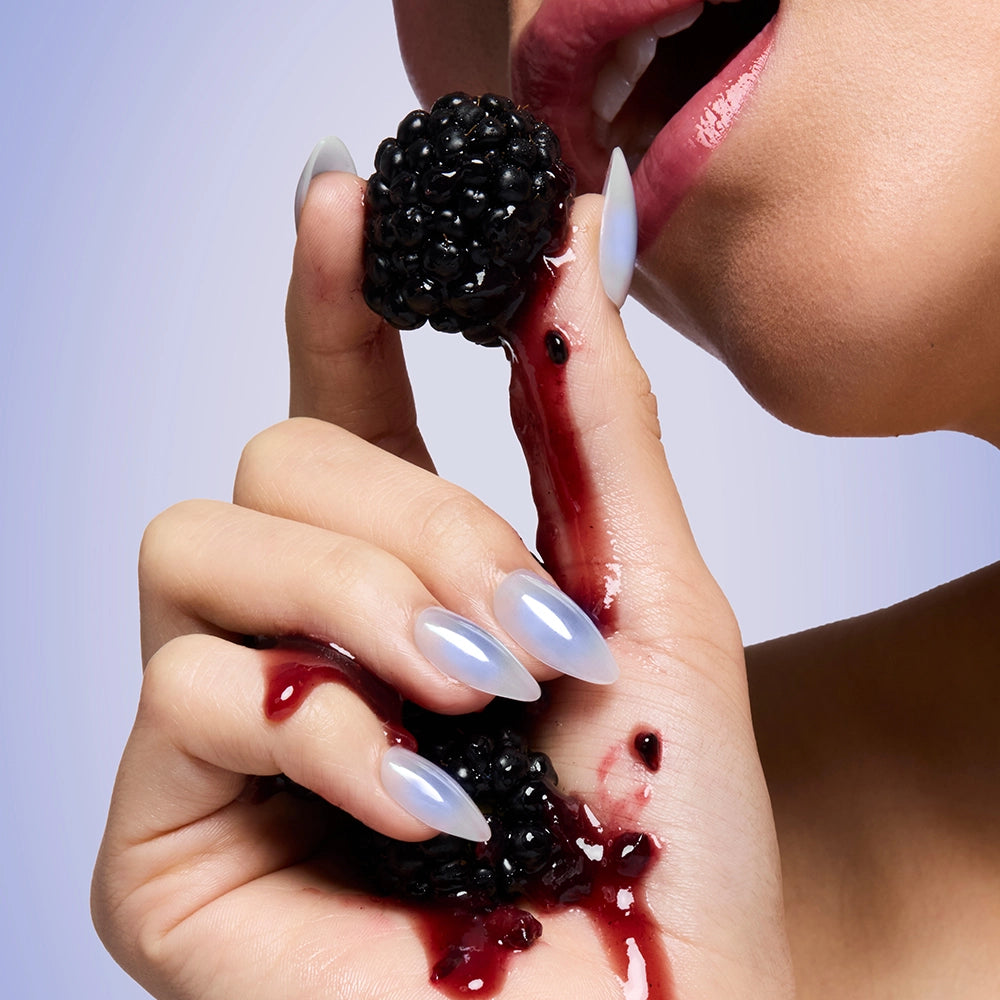 A close-up features glossy lips and long, almond nails in glamnetic’s Sky Berry—a shiny pale blue—dripping with blackberry juice against a soft gradient light blue background. - Product image