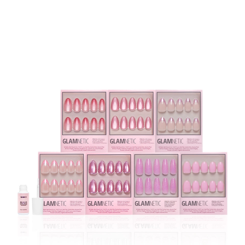 Eight boxes from the glamnetic Soft Launch Bundle are arranged in various pink and nude shades and finishes, including a stunning pink set and sleek chrome nails. A small white nail glue bottle sits to the left of the boxes. - Product image