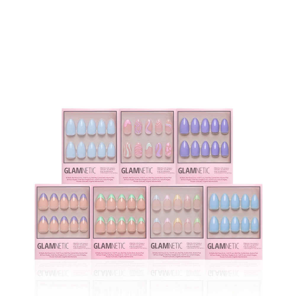 Eight boxes of glamnetic Almond Blossom press-on nails are displayed in two rows, each with a unique pastel glossy set—blue, pink, purple, nude, or playful designs—in chic pink packaging. - Product image