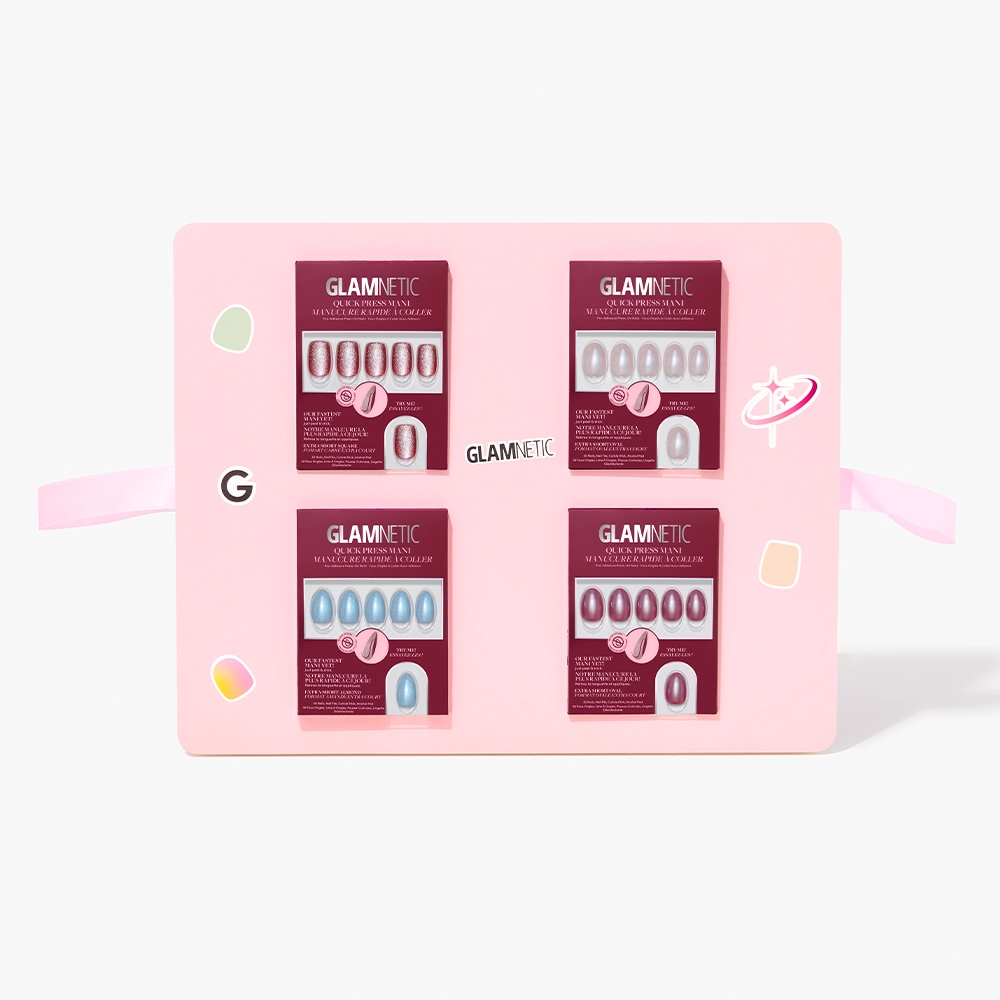 A pink display board showcases four sets of glamnetic Quick Press Mani PR Box no-glue press-on nails in burgundy packaging, arranged in a grid and decorated with colorful accents and two pink ribbons on each side. - Product image