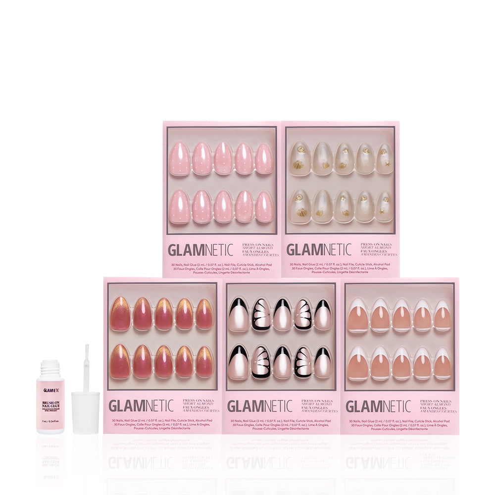 Five boxes of glamnetic Almond Atelier nail sets in pink, nude, and decorative styles are stacked in two rows. An open bottle of nail glue with a brush sits to the left of the chic bundle on a white background. - Product image