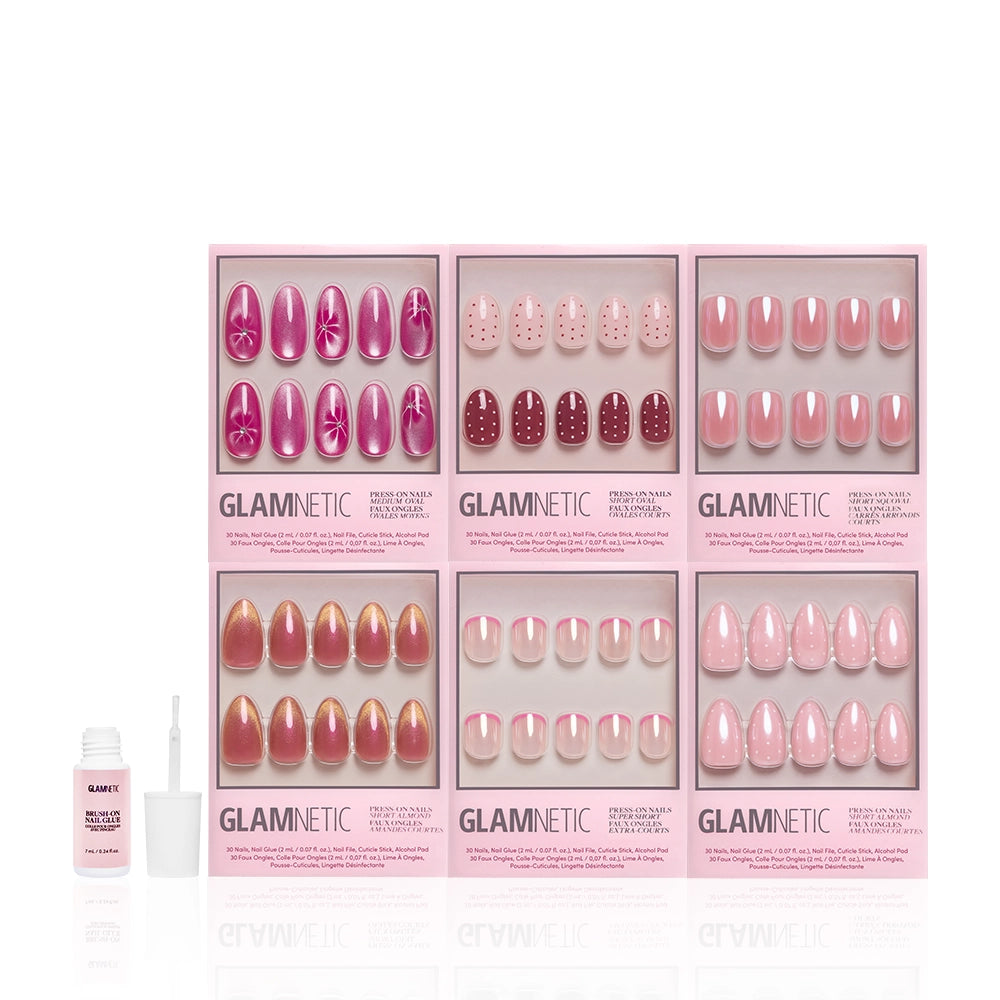 Six boxes of glamnetic Blush Dusted press-on nails in spring pink, featuring florals, polka dots, glossy, glazed, and French tips. An open bottle of nail glue with a brush on the left ensures easy application. - Product image