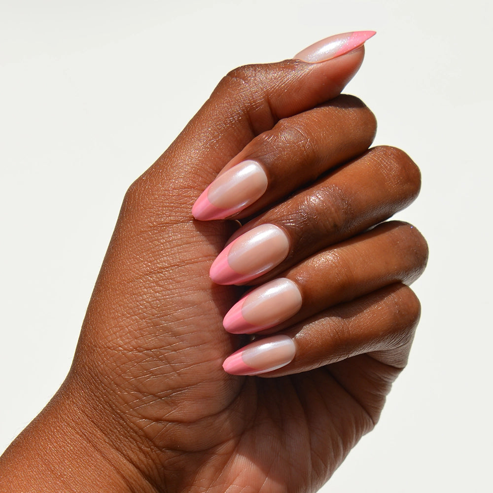 A hand with glamnetic Bubble Gum Glaze short almond press-on nails, featuring a glossy light pink base and bright glazed French tips, is shown against a plain white background.