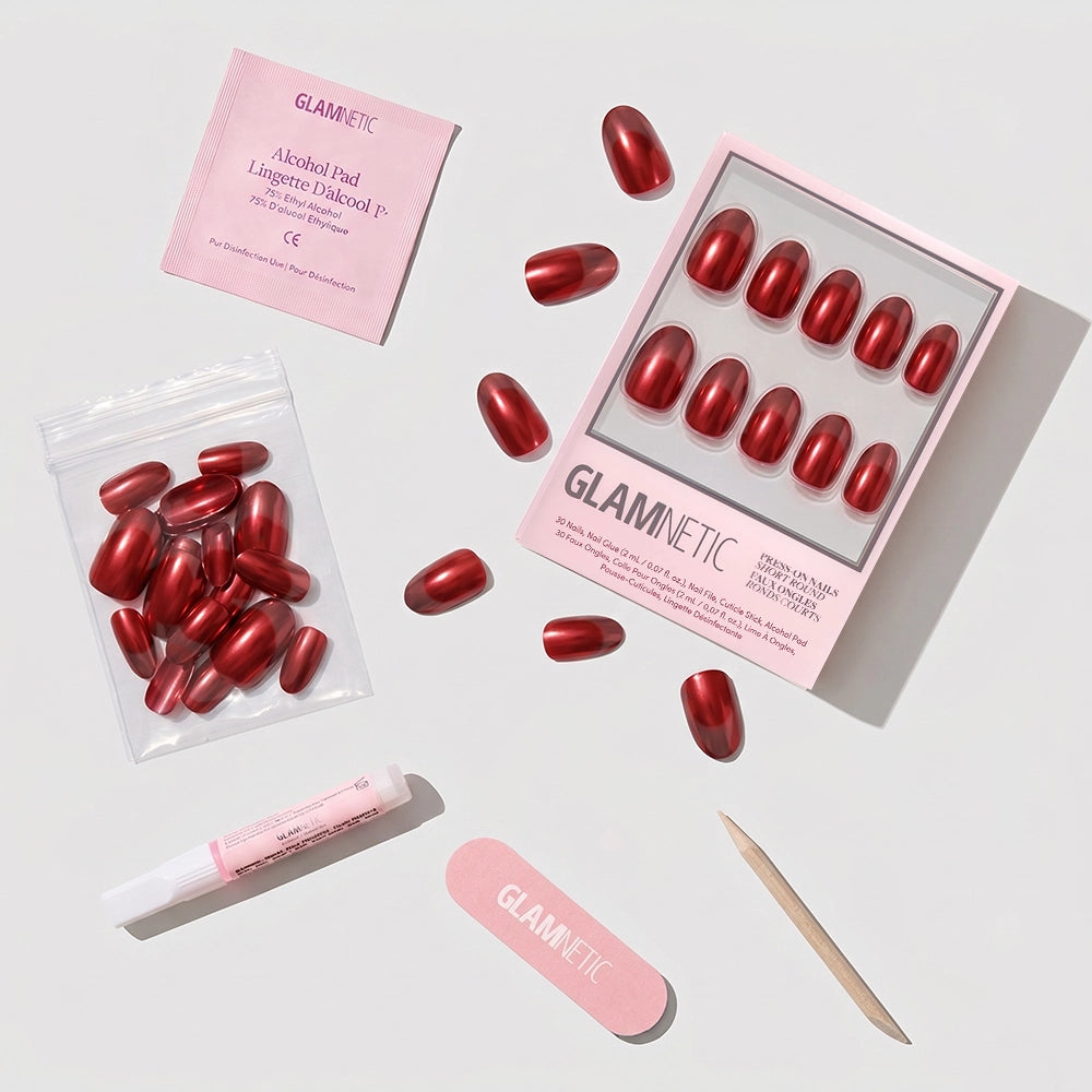 The glamnetic Cherry Glaze set includes red short round press-on nails, nail glue, an alcohol pad, a mini nail file, a cuticle stick, and extra nails, all arranged neatly on a white surface. - Product image