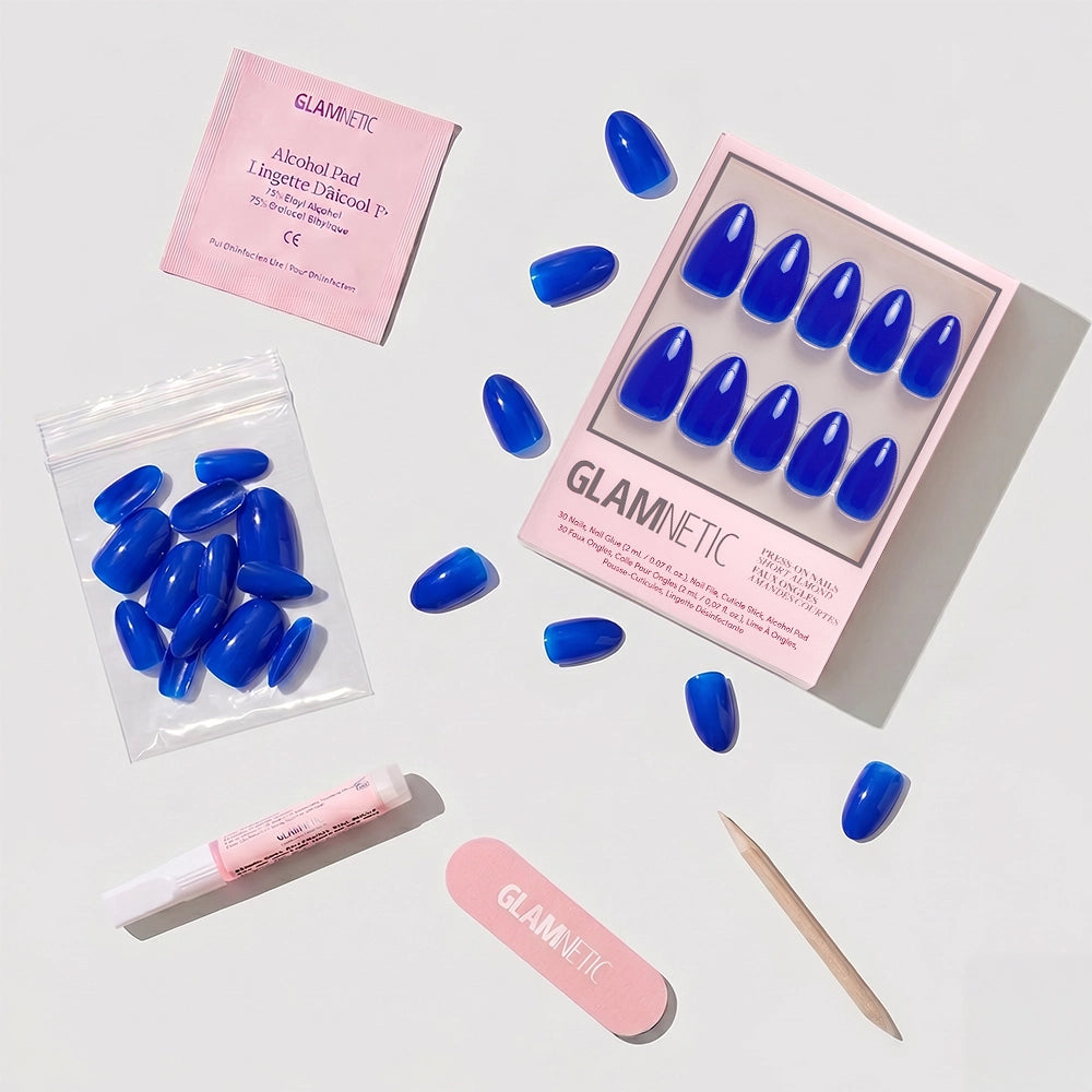 The glamnetic Cobalt Blue set includes short almond press-on nails, a pink nail file, cuticle stick, glue, alcohol pad, and extra nails—perfectly arranged for a chic summer manicure. - Product image