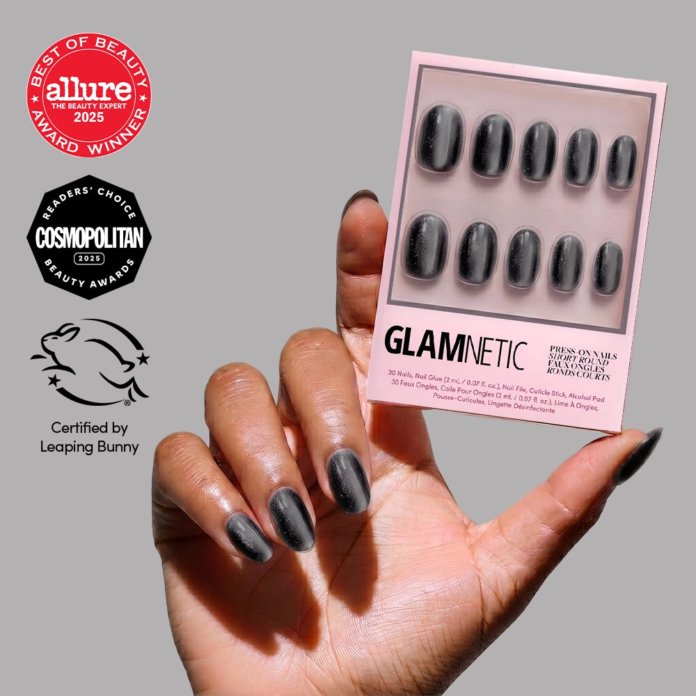 A hand with shiny, black short round nails holds a box of glamnetic Galactic press-on nails, featuring Allure, Cosmopolitan, and Leaping Bunny awards and certifications on the side.