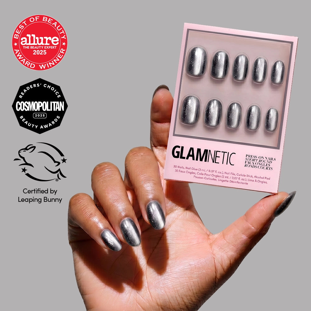 A hand with metallic silver Galactic press-on nails holds a glamnetic box. Award badges from Allure, Cosmopolitan, and the Leaping Bunny cruelty-free logo highlight this vegan nail set.