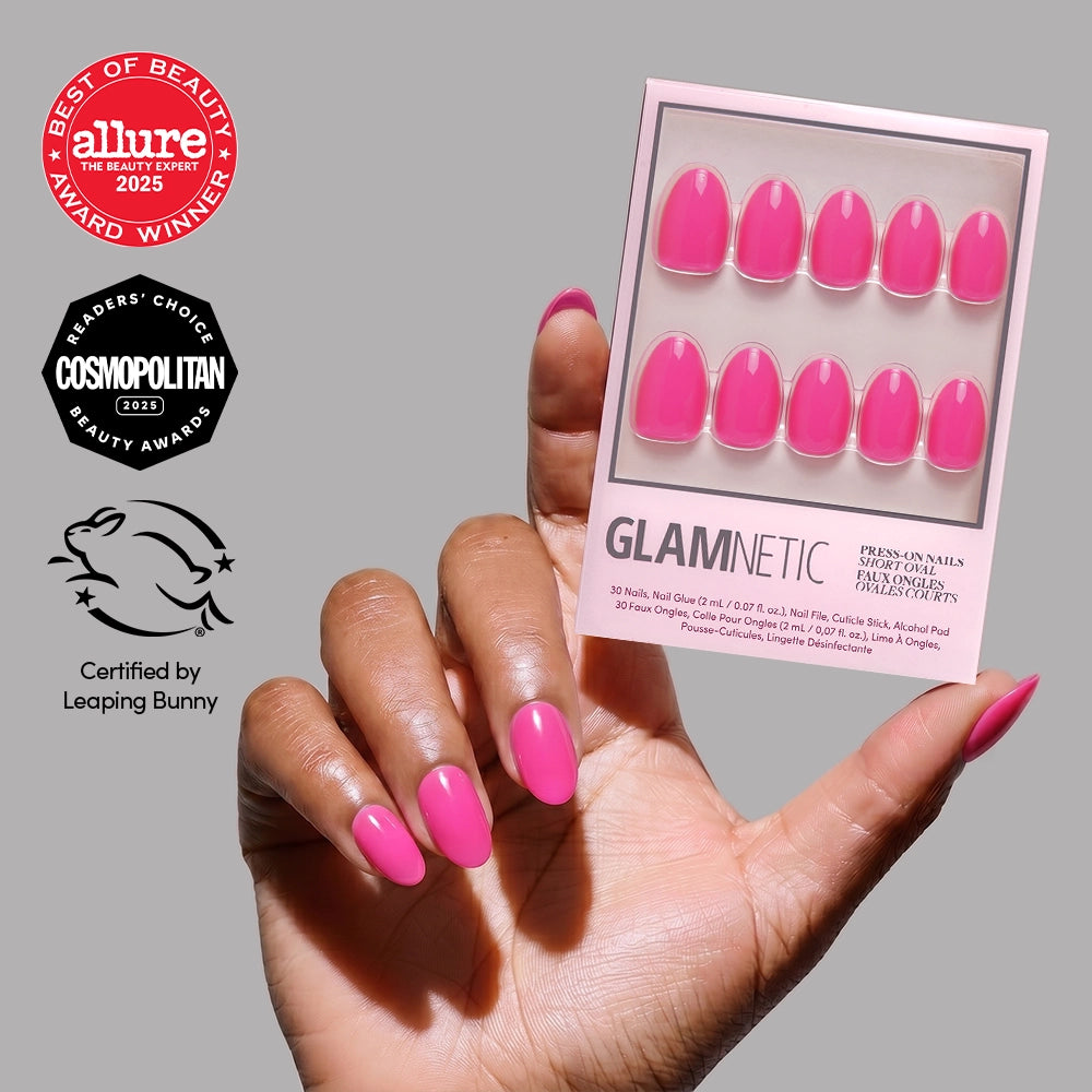 A hand with hot pink nails holds glamnetic’s “Hot Pink” short oval press-on nail set. Allure, Cosmopolitan, and Leaping Bunny award badges appear on the left against a neutral background—perfect for chic summer nails.