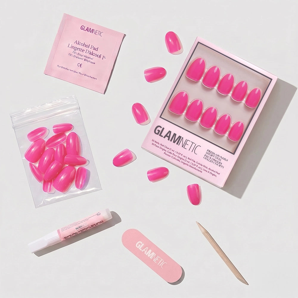 A flat lay of glamnetic Hot Pink short oval press-on nails set, including a nail file, cuticle stick, alcohol pad, nail glue tube, and extra nails—ideal for summer nail designs on a light background. - Product image