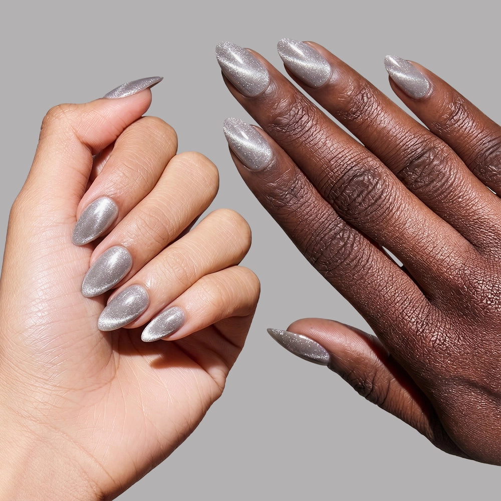 Two hands, one light-skinned and one dark-skinned, display glamnetic’s Oslo short almond press-on nails in a metallic silver cat-eye finish against a plain gray background. - Product image