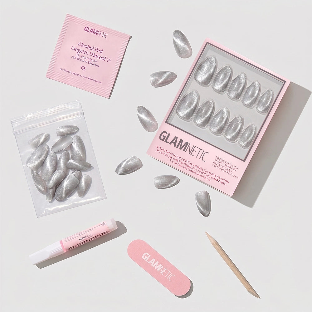 A set of Oslo silver cat-eye nails, an alcohol pad, nail glue, a pink nail file, a wooden cuticle stick, and extra nails are arranged on a white surface; pink glamnetic branding is visible on the box, pad, and nail file. - Product image