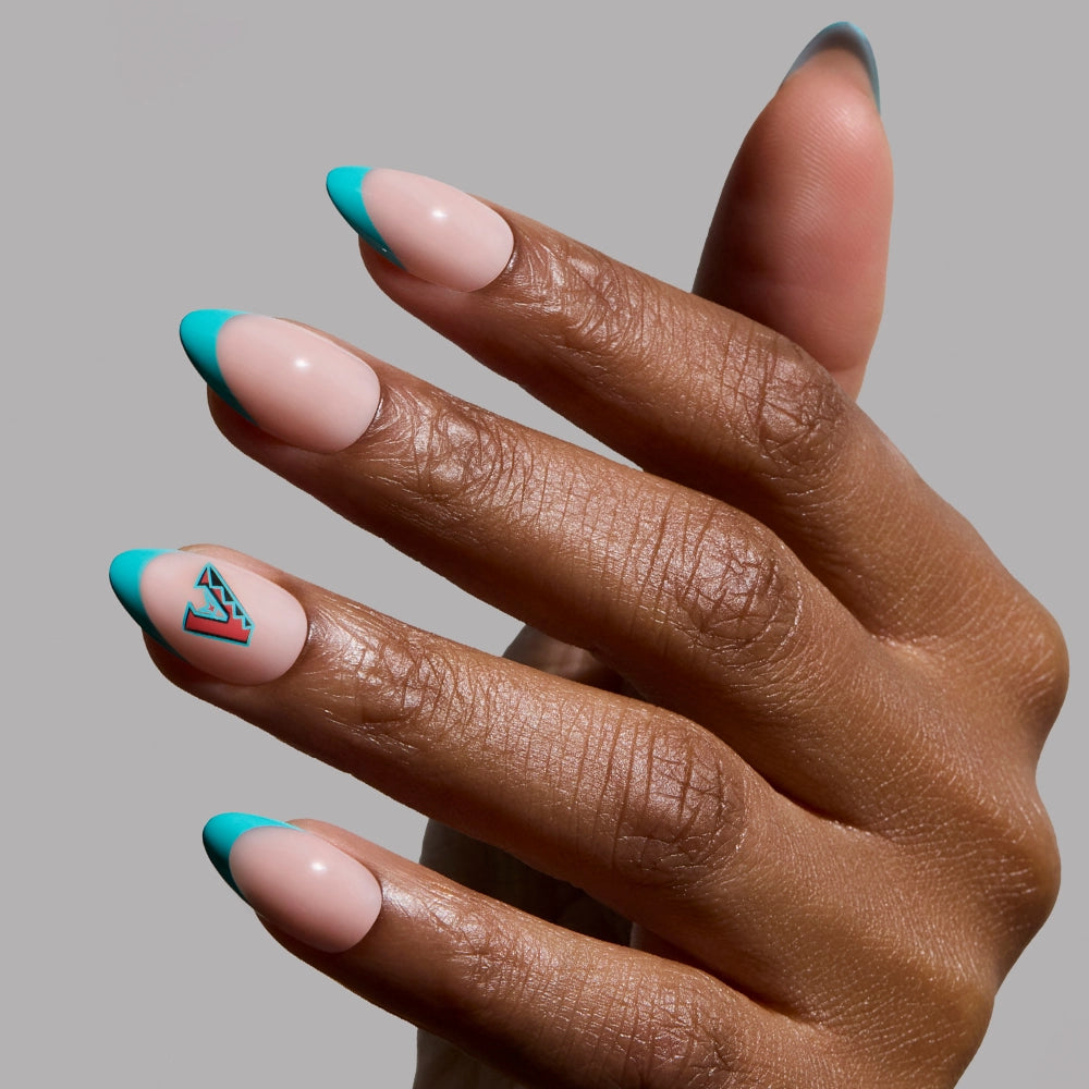 A hand shows off the glamnetic Arizona Diamondbacks Press-On Nail Set: short almond nails with a nude base and turquoise French tips, plus a turquoise geometric triangle on the ring finger. The background is light gray.