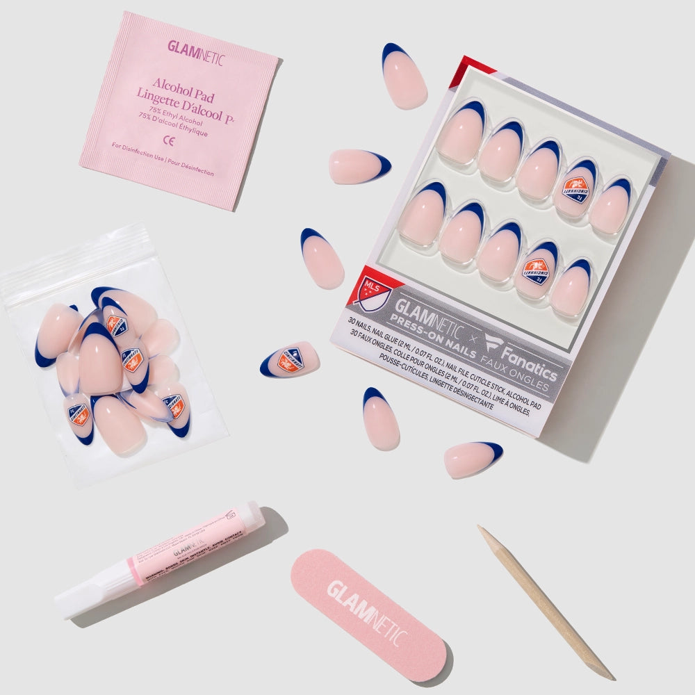 A flat lay of the glamnetic FC Cincinnati Press-On Nail Set featuring almond nails with pink and blue tips, extra vegan press-ons in a pouch, an alcohol pad, nail glue, a pink file, and a wooden cuticle stick on a light background. - Product image