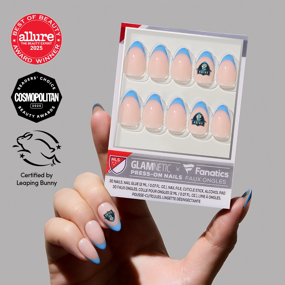 A hand showcases glamnetic’s Philadelphia Union Press-On Nail Set with blue tips and a soccer logo. The box appears next to short almond nails, alongside Allure and Cosmopolitan award seals and Leaping Bunny certification.