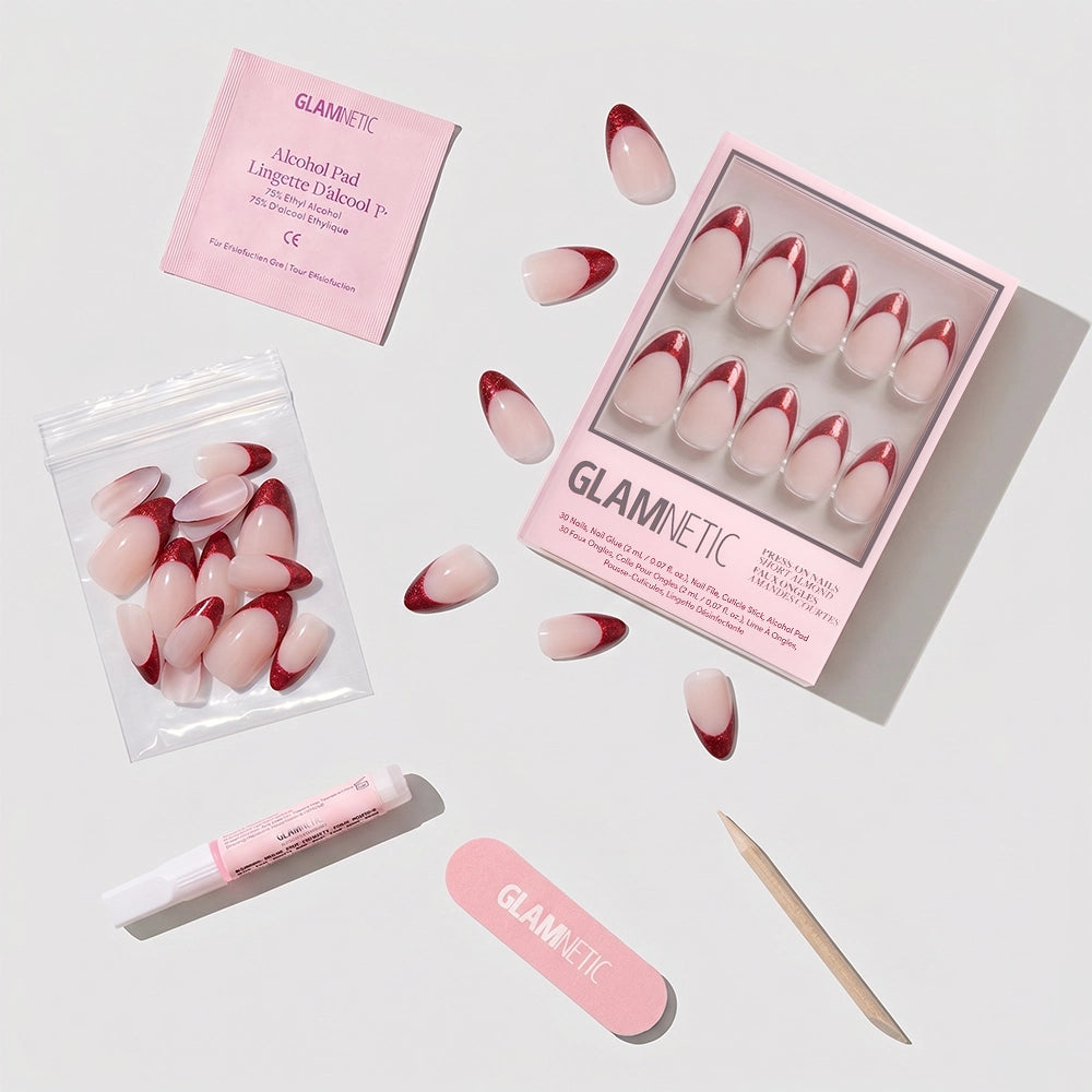 The glamnetic Red Affair press-on nail kit includes short almond nails with red glitter French tips, extra nails, an alcohol pad, nail glue, a pink file, and a cuticle stick—all displayed on a white background. - Product image