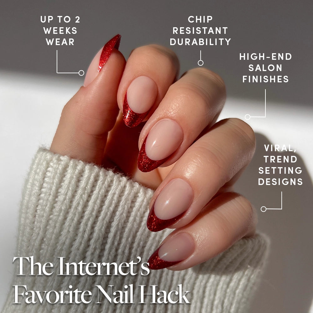 A hand with short almond Red Affair press-on nails by glamnetic, boasting nude polish and red glitter French tips, paired with a white sweater. Enjoy up to 2 weeks wear, chip resistance, salon-quality finishes, and trendy designs—perfect for any occasion. - Product image