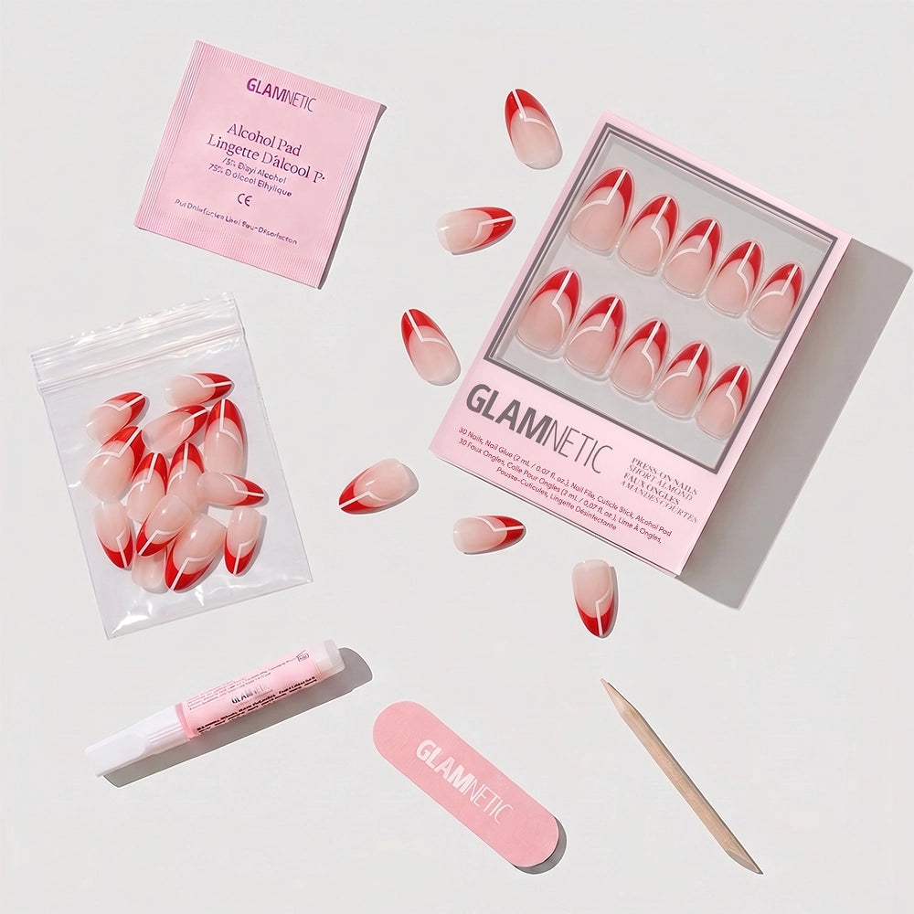 The glamnetic Red Martini holiday press-on nails feature a red and nude French tip design, shown with an alcohol pad, glue tube, mini nail file, wooden cuticle stick, and extra short almond nails on a light background. - Product image