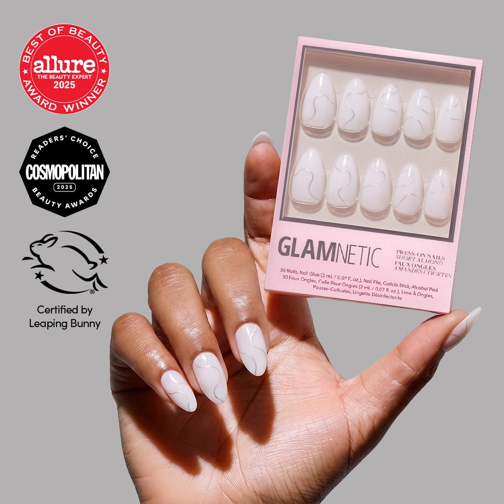 A hand shows off Silent Night by glamnetic—glossy white, short almond vegan press-on nails with thin wavy gray lines—while holding the box. Allure, Cosmopolitan, and Leaping Bunny certification logos appear on the left. - Product image