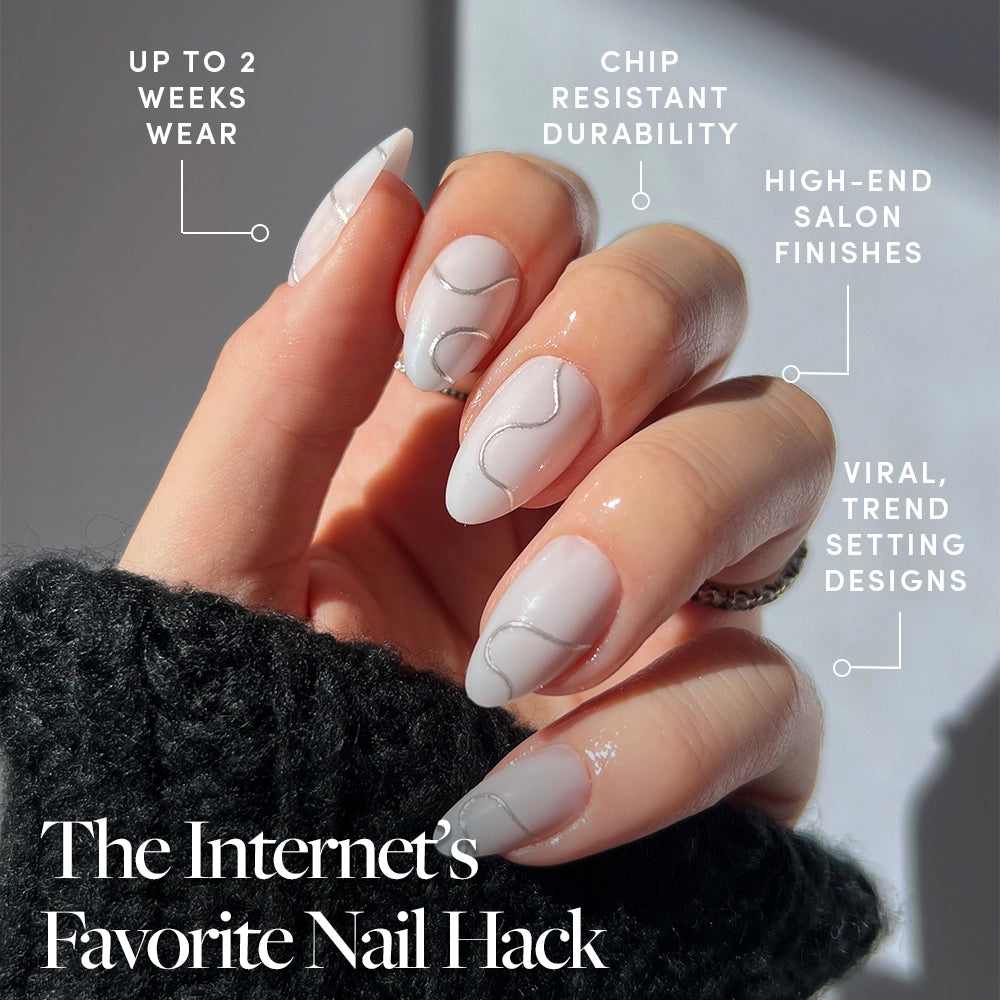 A hand with long, manicured glamnetic Silent Night press-on nails features a minimalist white and silver swirl design. Benefits: up to 2 weeks wear, chip-resistant durability, salon-quality finish, and viral trendsetting style. - Product image