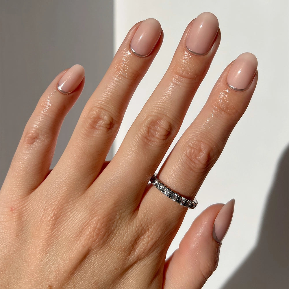 A hand with neatly manicured, short round nails models the glamnetic Silver Belle ring—silver with small, sparkling stones on the ring finger—against a neutral background.