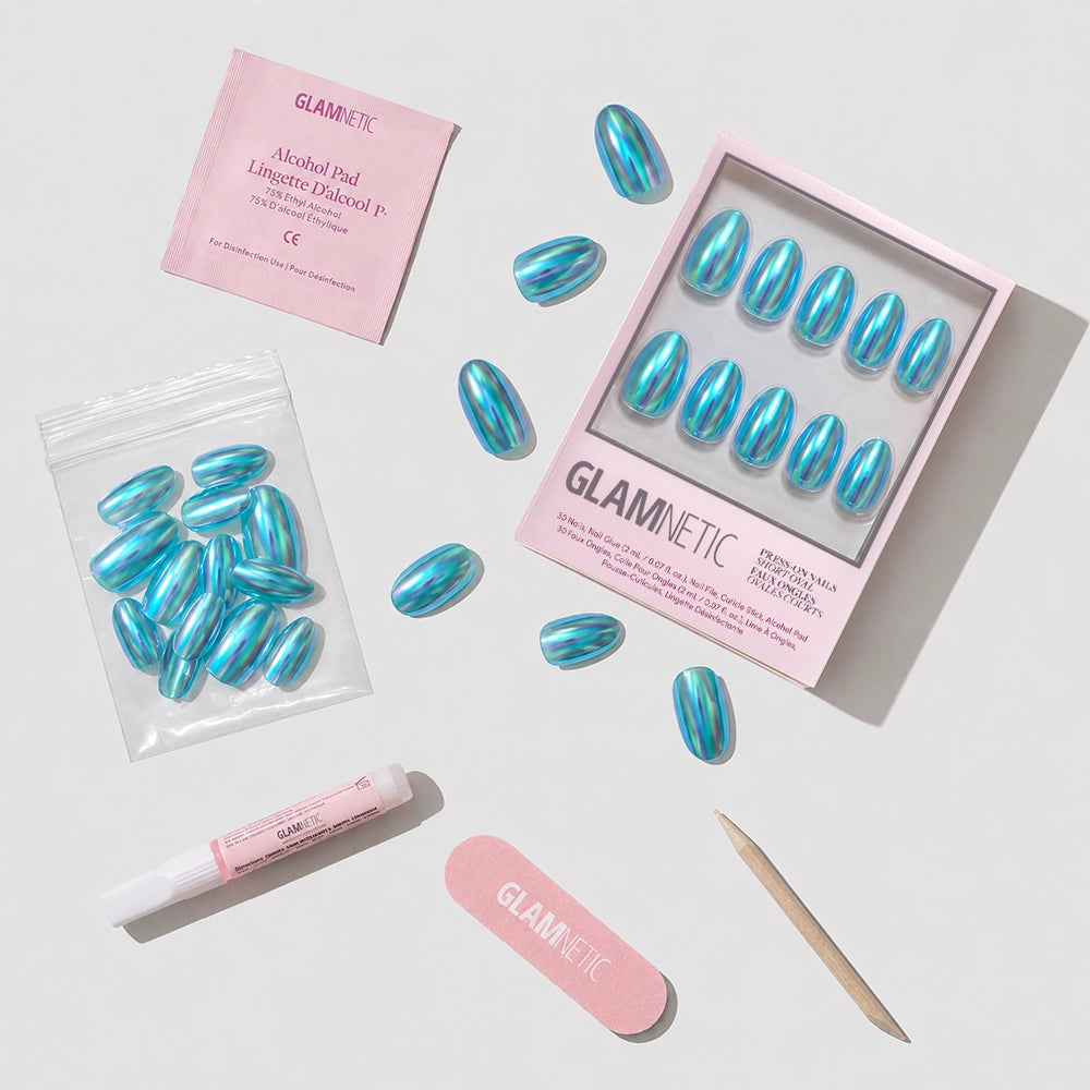 The Siren Nail Set by glamnetic includes blue and silver striped holographic short oval press-ons, plus a nail file, wooden cuticle stick, glue tube, alcohol pad, and extra adhesive tabs presented on a white surface. - Product image