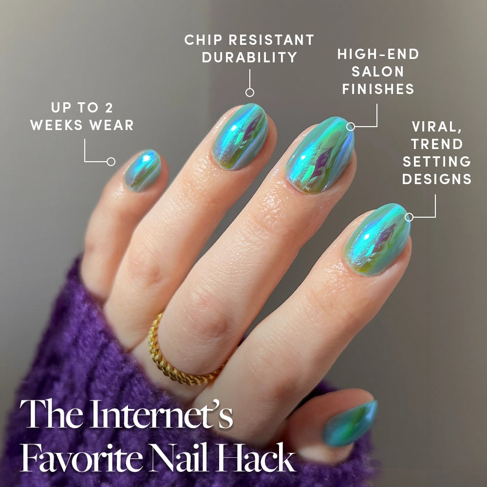 A hand with glamnetic Siren press-on nails—shiny, iridescent green and blue holographic—shows off up to 2 weeks wear, chip-resistant durability, salon-quality finish, and viral trendsetting style. The person wears a gold ring and purple sweater. - Product image