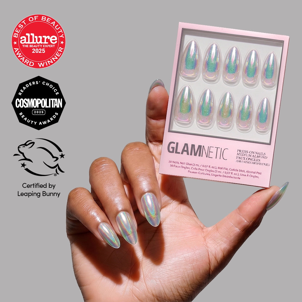 A hand with long, iridescent glamnetic press-on nails in the shade "Stardust" holds the box. Award badges from Allure, Cosmopolitan, and Leaping Bunny certification are displayed to the left of the hand.