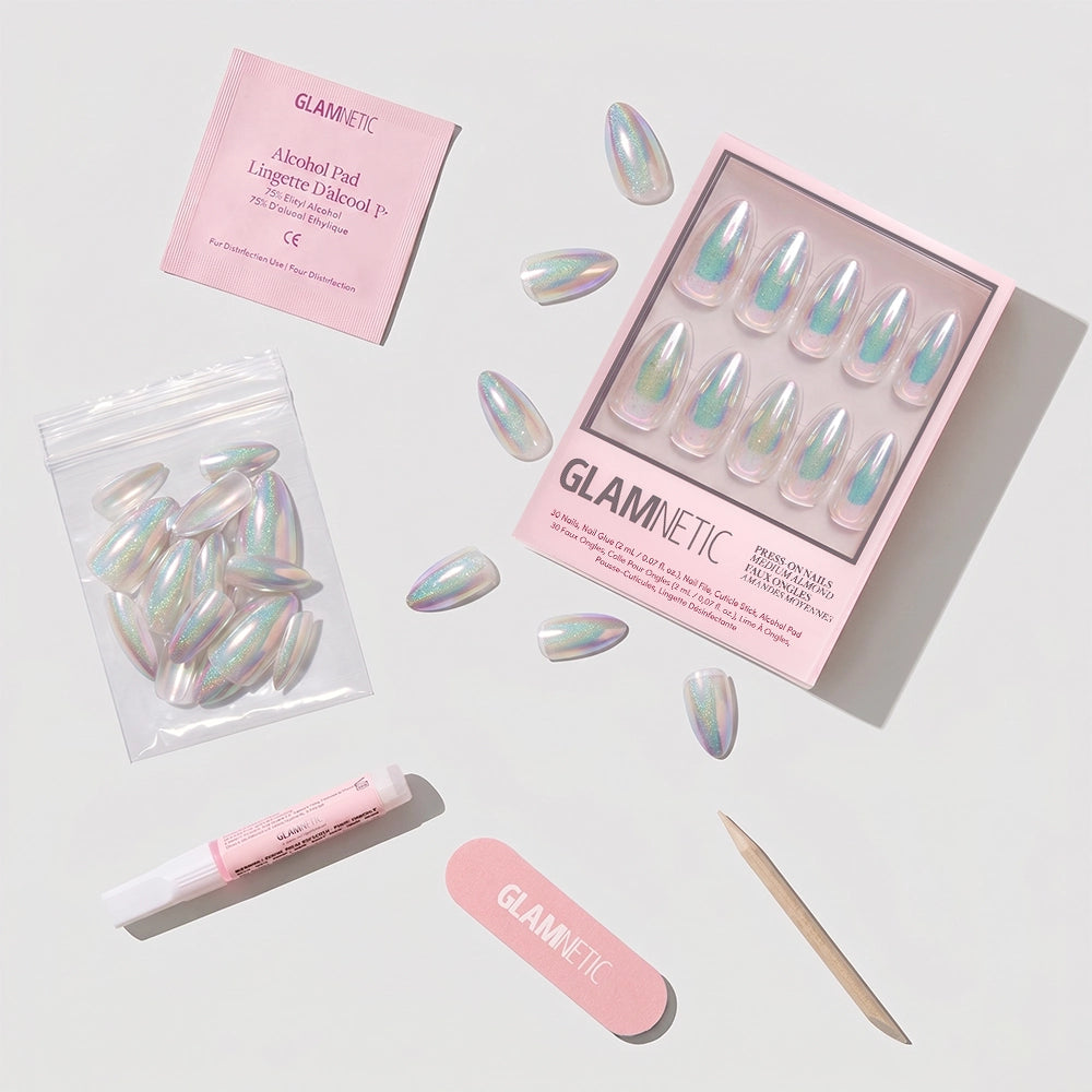 The glamnetic Stardust set features iridescent almond press-on nails in a pink box, complete with an alcohol pad, extra nails in a small bag, nail glue, a pink file, and a wooden cuticle stick on a white surface. - Product image