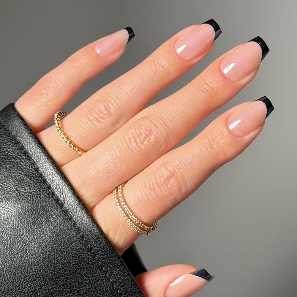 A hand with long, coffin-shaped nails shows off glamnetic's Balsamic Glaze French manicure with black tips. Two gold rings and a black leather sleeve partially cover the hand. - Product image
