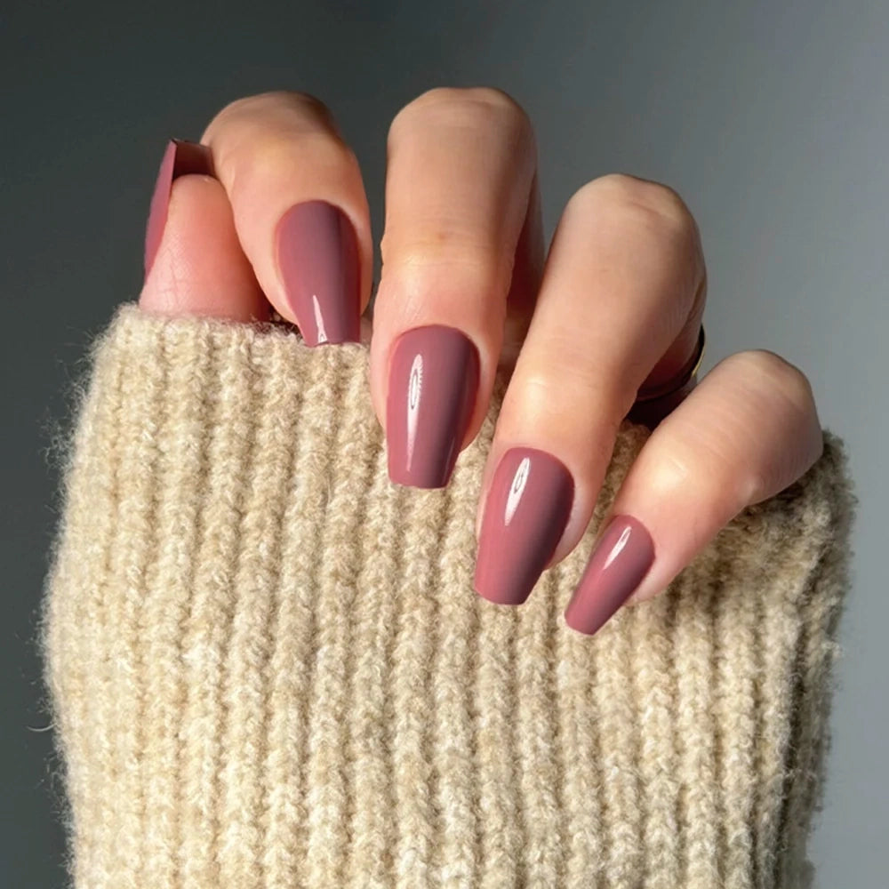 A hand showcases glamnetic's Mauve Affair press-on nails in a long, glossy coffin shape. The wearer’s beige ribbed sweater highlights the chic, mauve-toned manicure against a softly lit, plain background. - Product image