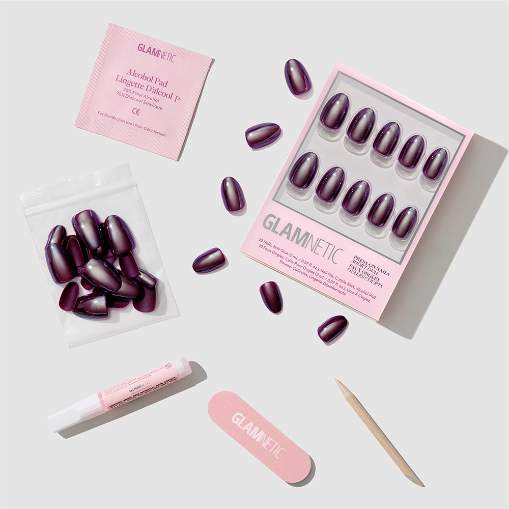 The “After Hours” dark purple short oval press-on nails by glamnetic feature a glazed finish and come with glue, an alcohol pad, nail file, wooden cuticle stick, and extra nails, all arranged neatly on a light gray background. - Product image