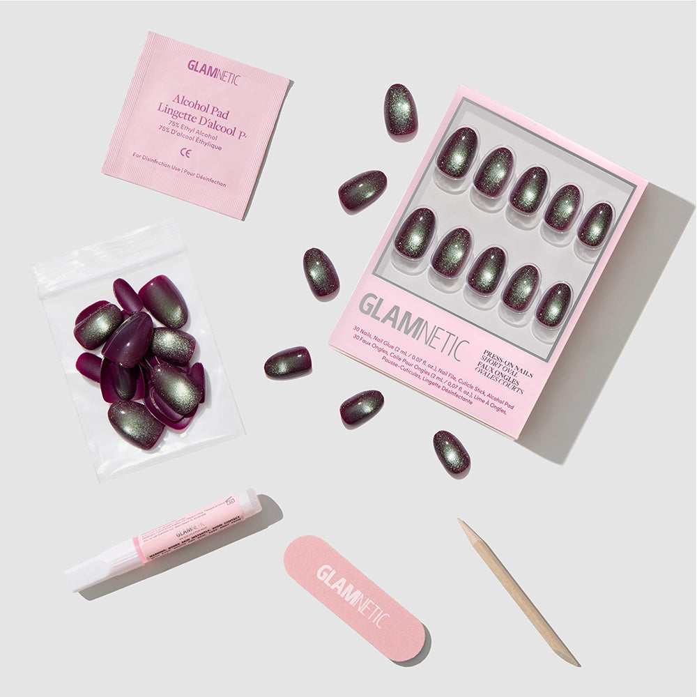 Introducing Alakazam by glamnetic—a press-on nail kit featuring short oval nails in stunning purple and green shades with a plush velvet finish. The set comes complete with an alcohol pad, nail glue, file, cuticle stick, and extra press-on nails, all elegantly displayed on a light gray background. - Product image