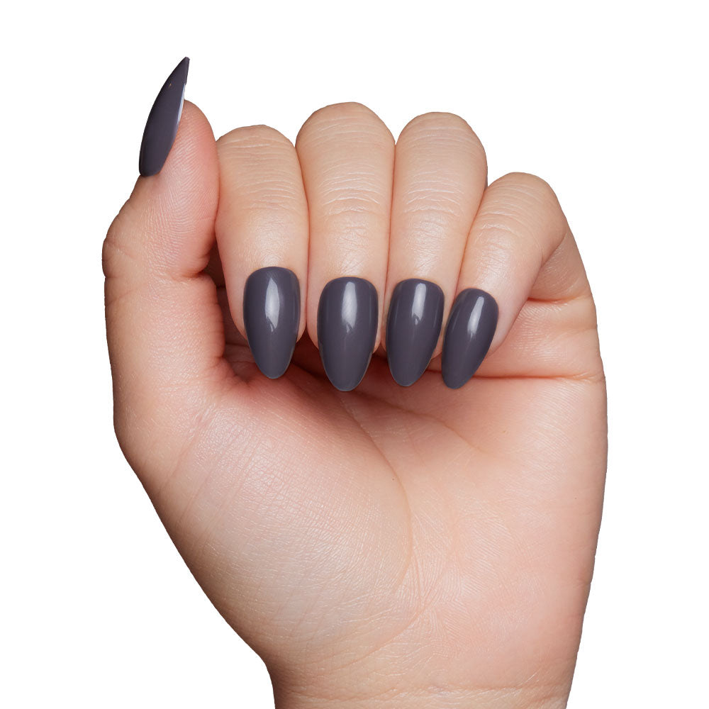 A medium skin tone hand displays long, almond nails from glamnetics Ash Gray set, painted in glossy dark gray. The fingers curl inward, and the neatly manicured nails are part of the Fall Forest Collection. - Product image