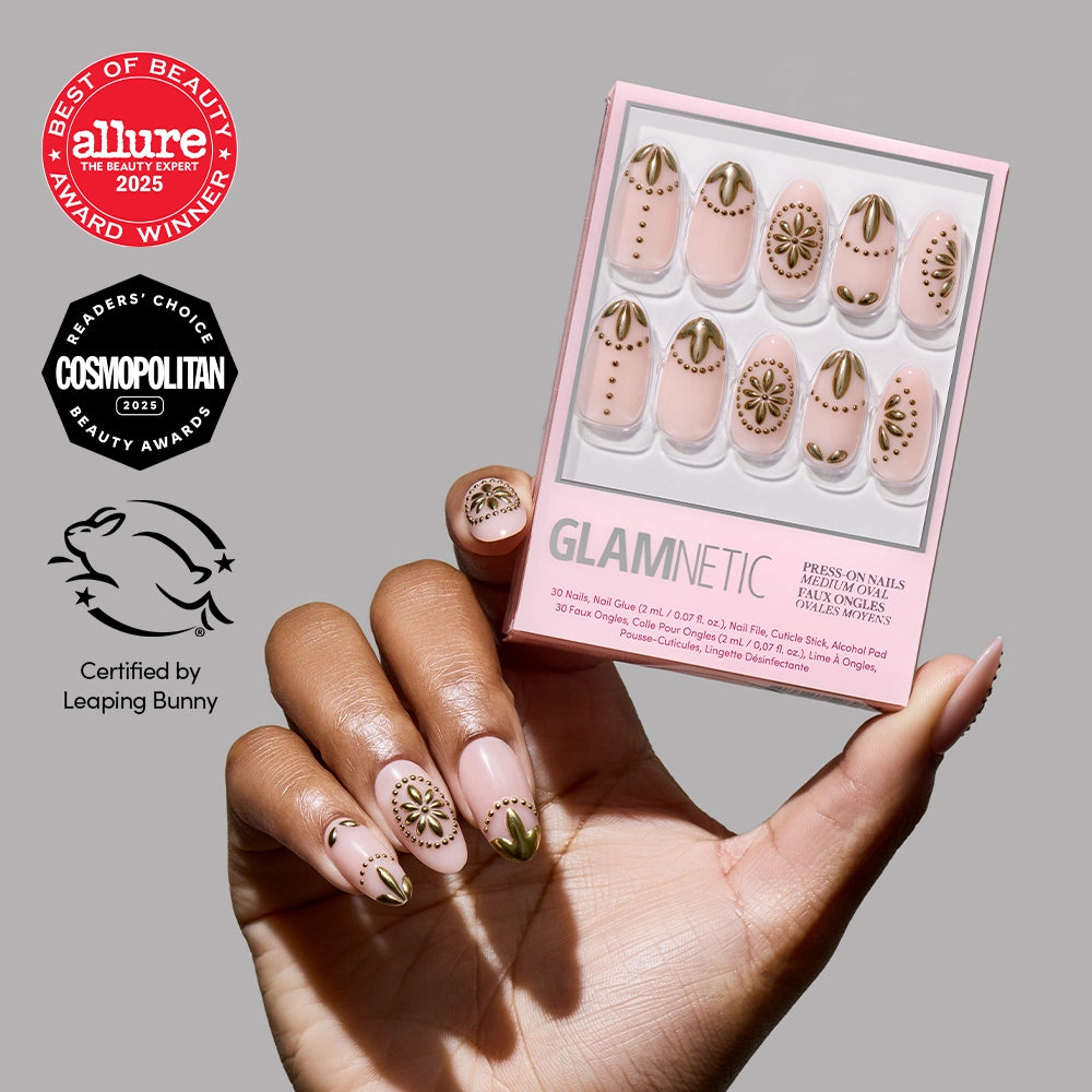 A hand with gold and pink glamnetic Athenian Gold press-on nails holds a box of matching salon-quality nails, featuring gold geometric designs. Allure, Cosmopolitan, and Leaping Bunny cruelty-free logos appear on a gray background.
