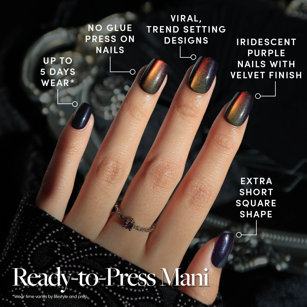 A hand with extra short, square iridescent purple press-on nails with a velvet finish, styled in the Aura Reading Quick Press Mani. Text labels highlight viral designs, no-glue nails for easy application, and up to 5 days wear. The hand wears a ring and rests on a black fabric. - Product image