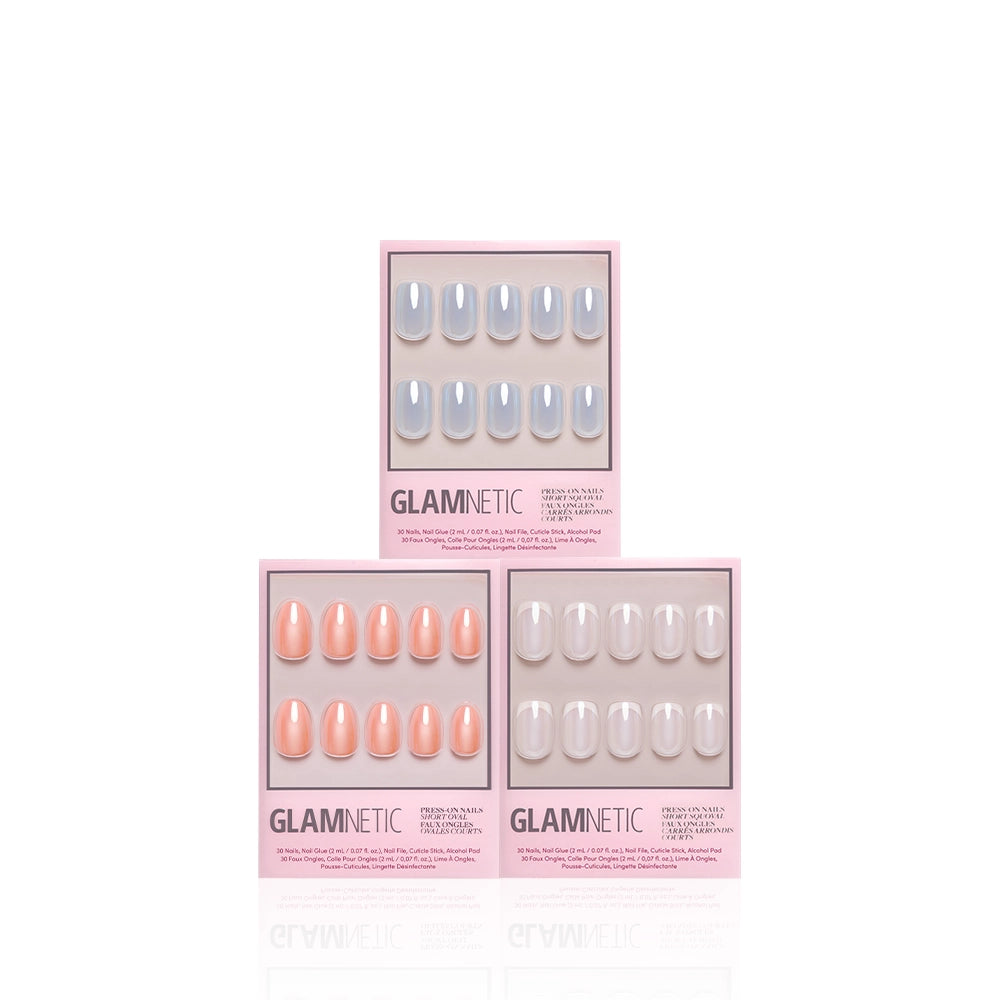 Three boxes of glamnetic Soft & Dreamy press-on nails are arranged in a triangle. The top box features gray nails, the bottom left displays peach nails, and the bottom right presents nude nails—all with a high-shine glazed finish. Each pink-and-white package adds an extra touch of glamour to these salon-quality press-on nails. - Product image