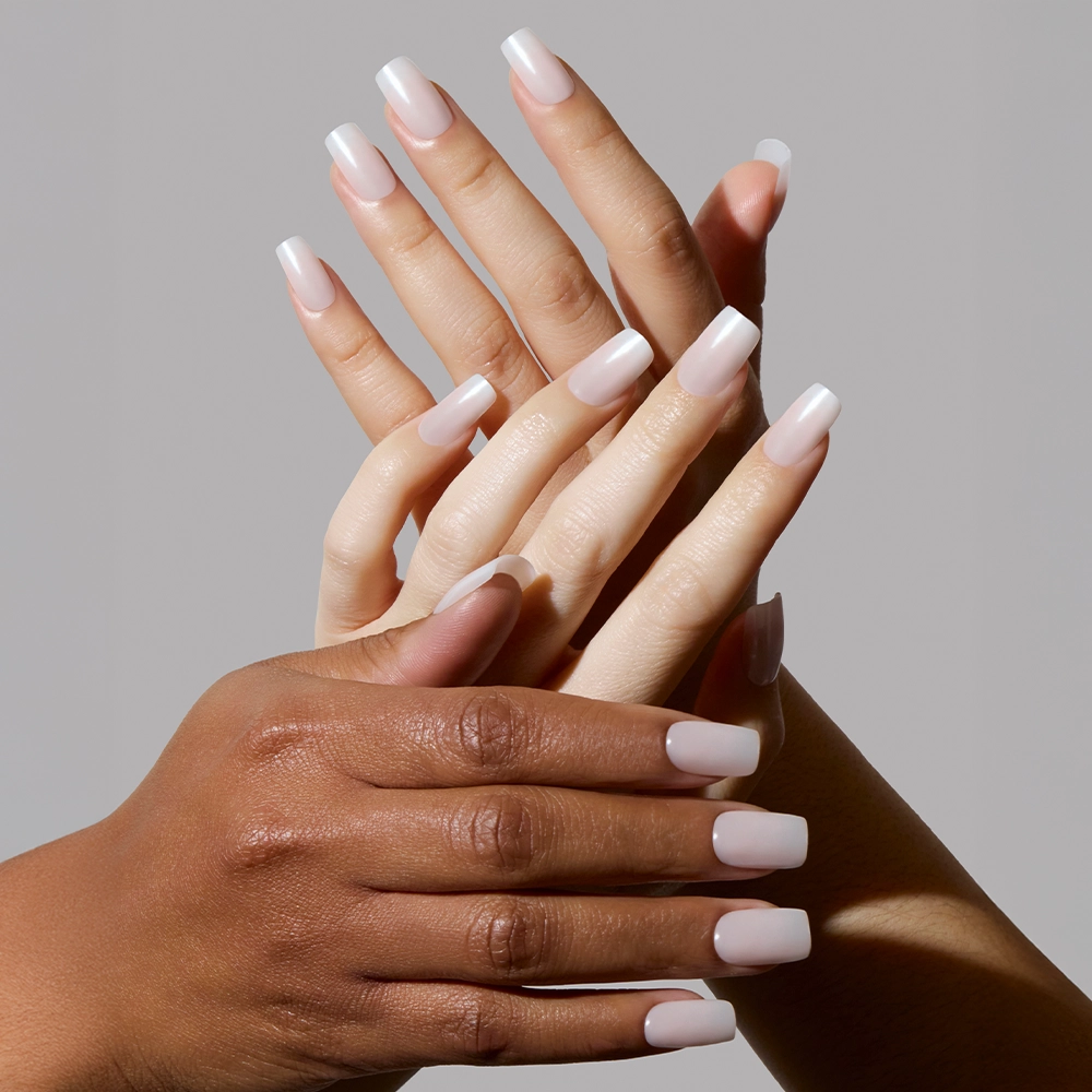 Two pairs of hands with different skin tones display Bailey medium square nails by glamnetic, featuring a glossy, semi-transparent light pink finish, posed gracefully against a plain gray background. - Product image